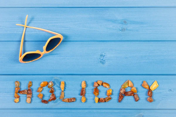 Word holiday made of amber stones and sunglasses on blue boards, summer time, copy space for text — Stock Photo, Image