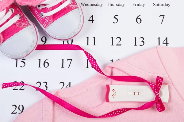 Schwangerschaftstest mit positivem Ergebnis und Kleidung für Neugeborene auf Kalender, Erwartung für Baby — Stockfoto