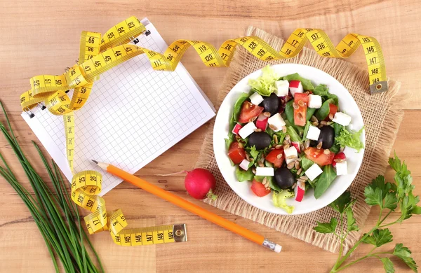 Čerstvý Řecký salát se zeleninou, centimetr a Poznámkový blok pro psaní poznámek, zdravé výživy a hubnutí koncepce — Stock fotografie