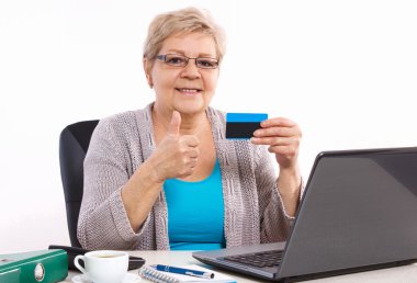 Yaşlı yaşlı kadın kredi kartı tutan ve başparmak gösteren, faturaları veya alışveriş için internet üzerinden ödeme
