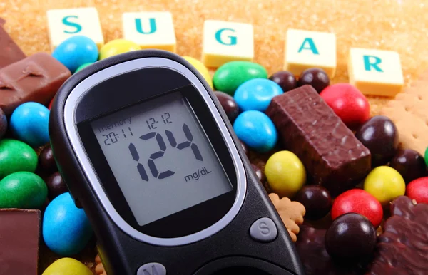 Glucosímetro, dulces y azúcar morena de caña con palabra azúcar, alimentos poco saludables — Foto de Stock