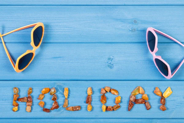 Word holiday made of amber stones and sunglasses on blue boards, summer time, copy space for text — Stock Photo, Image