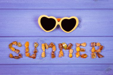 Word summer made of amber stones and sunglasses on purple boards, summer time