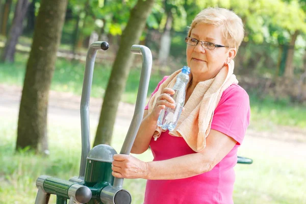 Старшая женщина питьевая вода после тренировки на открытом воздухе тренажерный зал, здоровый образ жизни — стоковое фото