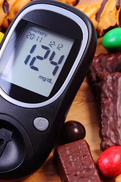Glucometer com montão de doces na superfície de madeira, diabetes e alimentos insalubres — Fotografia de Stock
