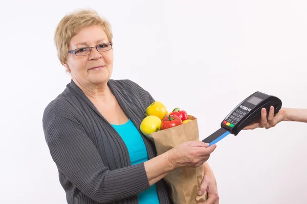 Mujer mayor sosteniendo bolsa de compras y usando terminal de pago con tarjeta de crédito, sin efectivo pagando por las compras — Foto de Stock