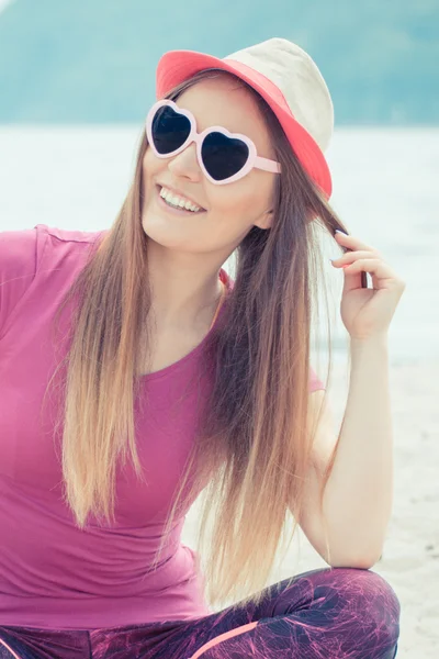 Chica feliz turista en sombrero de paja y gafas de sol sentado en la playa, tiempo libre en la playa — Foto de Stock