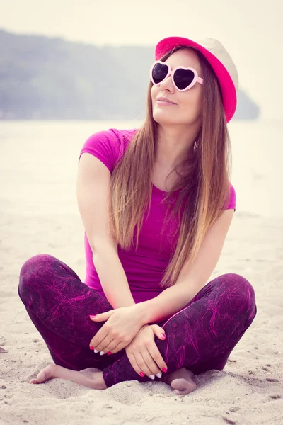 Chica feliz turista en sombrero de paja y gafas de sol sentado en la playa, tiempo libre en la playa — Foto de Stock