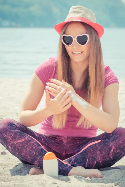 Happy girl in straw hat and sunglasses using sun lotion, sun protection on beach — Stock Photo, Image