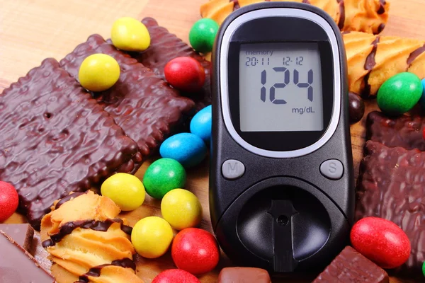 Glucometer with heap of sweets on wooden surface, diabetes and unhealthy food — Stock Photo, Image