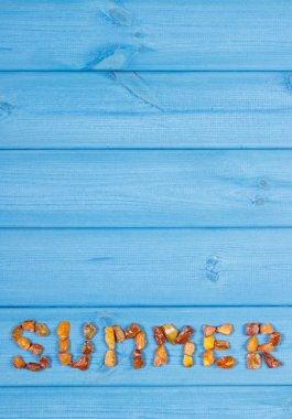 Word summer made of amber stones on blue boards, summer time, copy space for text
