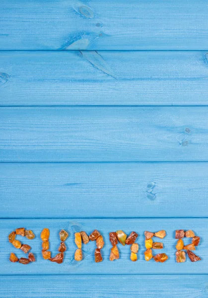 Word summer made of amber stones on blue boards, summer time, copy space for text