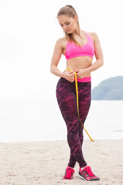 Slim girl in sporty clothes with centimeter on beach, sports lifestyle, slimming concept