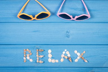 Word relax made of seashells, sunglasses on blue boards, summer time, copy space for text