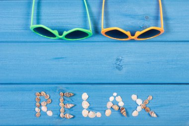 Word relax made of seashells, sunglasses on blue boards, summer time, copy space for text