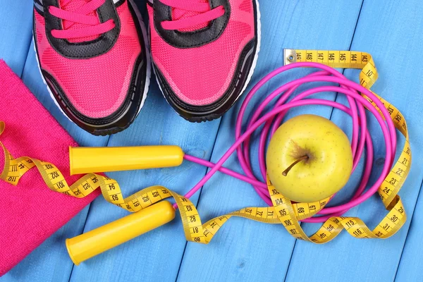 Pair of sport shoes, fresh apple and accessories for fitness on blue boards