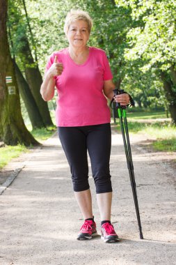 Yaşlı kadın kıdemli Nordik yürüyüş ve başparmak yukarıya, sportif yaşam gösterilen pratik