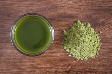 Young powder barley with cup of beverage on wooden background