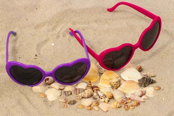 Un mucchio di conchiglie e occhiali da sole sulla sabbia in spiaggia — Foto Stock