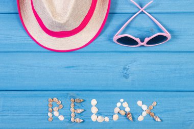 Word relax made of seashells, sunglasses and straw hat on blue boards, summer time, copy space for text