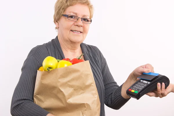 Mujer mayor sosteniendo bolsa de compras y usando terminal de pago con tarjeta de crédito sin contacto, pagando por las compras — Foto de Stock