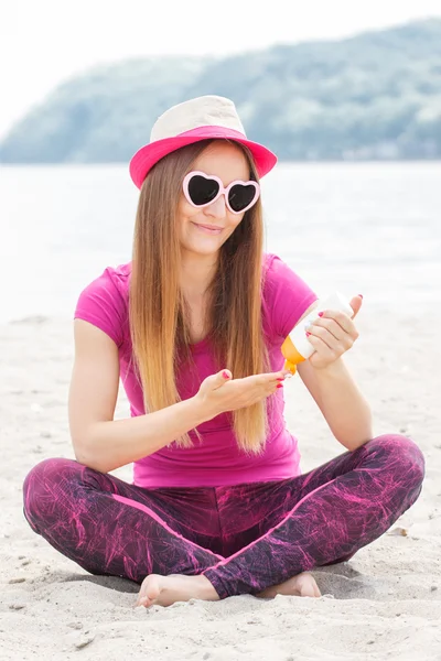 Chica feliz en sombrero de paja y gafas de sol con loción solar, protección solar en la playa — Foto de Stock