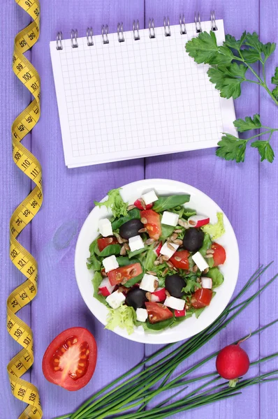 Greek salad with vegetables, centimeter and notepad for notes, healthy food and slimming concept