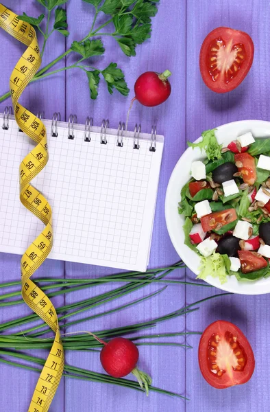 Greek salad with vegetables, centimeter and notepad for notes, healthy food and slimming concept