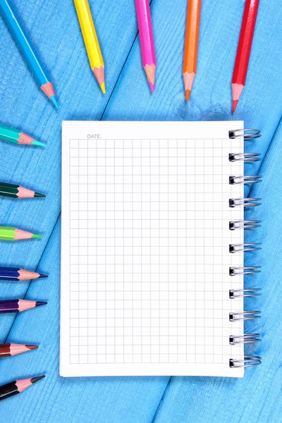 Colorful crayons and notepad on blue boards, school accessories, copy space for text — Stock Photo, Image