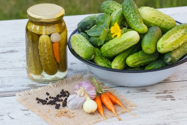 Gurkor i metall skål, kryddor för betning och burk saltgurka på bord — Stockfoto