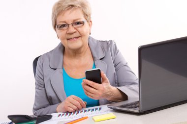 Cep telefonu kullaranarak ve ofis, iş kavramı masasında çalışan yaşlı bir iş kadını