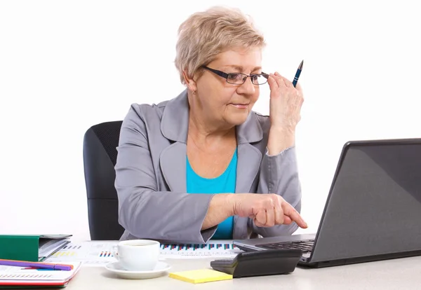 Пожилая деловая женщина, работающая с ноутбуком за своим столом в офисе, бизнес-концепция — стоковое фото