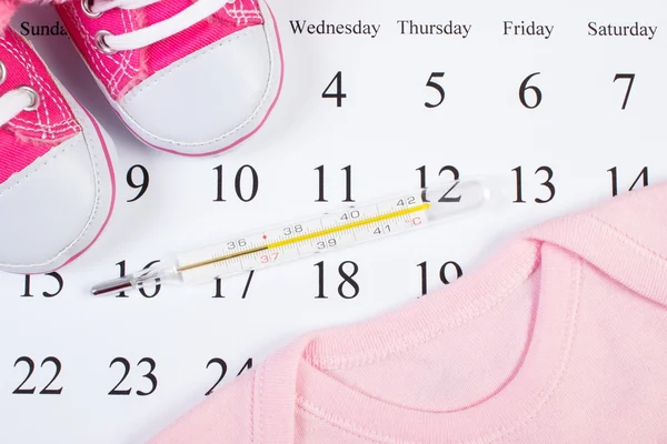 Thermometer und Kleidung für Neugeborene auf dem Kalender, Erwartung für Baby — Stockfoto