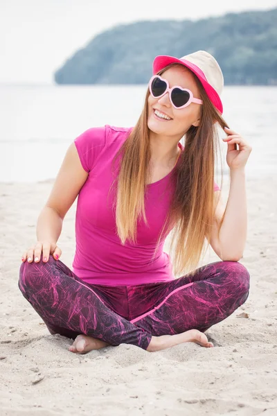 Chica feliz turista en sombrero de paja y gafas de sol sentado en la playa, tiempo libre en la playa — Foto de Stock