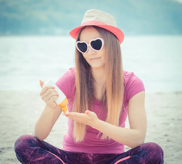 Chica feliz en sombrero de paja y gafas de sol con loción solar, protección solar en la playa — Foto de Stock