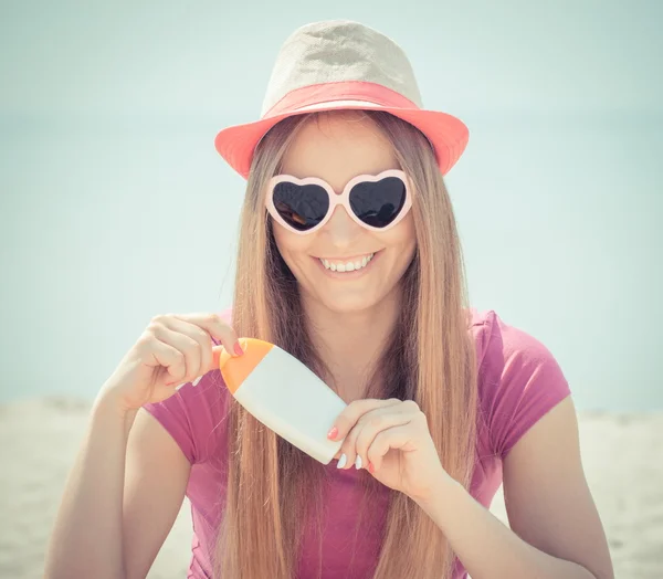 Chica feliz en sombrero de paja y gafas de sol con crema solar, protección solar en la playa — Foto de Stock