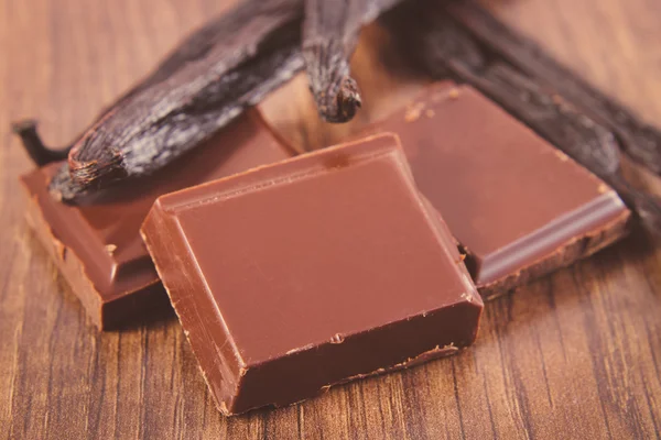 Chocolate escuro e palitos de baunilha perfumados na prancha de superfície de madeira — Fotografia de Stock