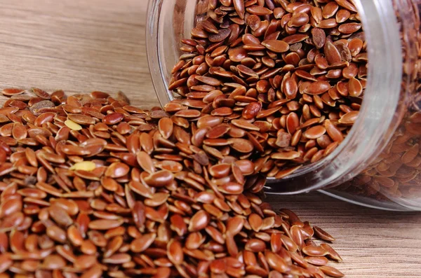 Linseed spilling out of jar on wooden background — Stock Photo, Image