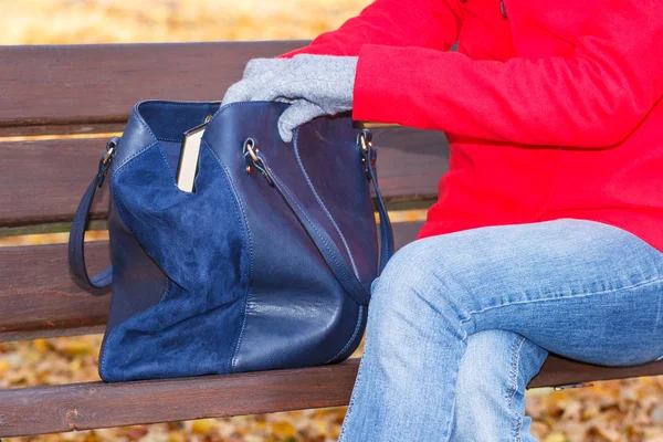 Woman sitting on bench in autum park and opening her handbag — Stock Photo, Image