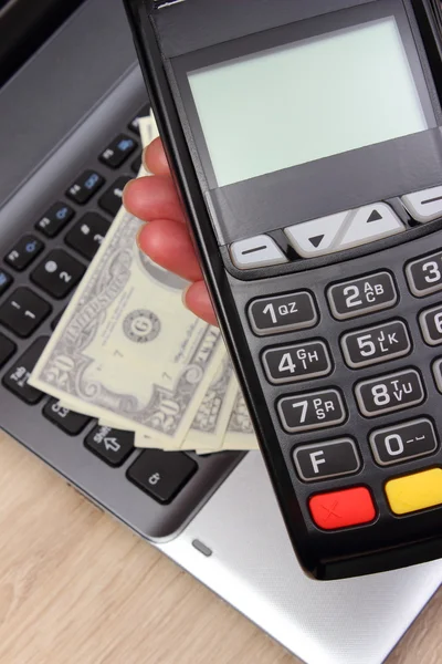 Hand of woman using payment terminal, currencies dollar on laptop in background — Stock Photo, Image