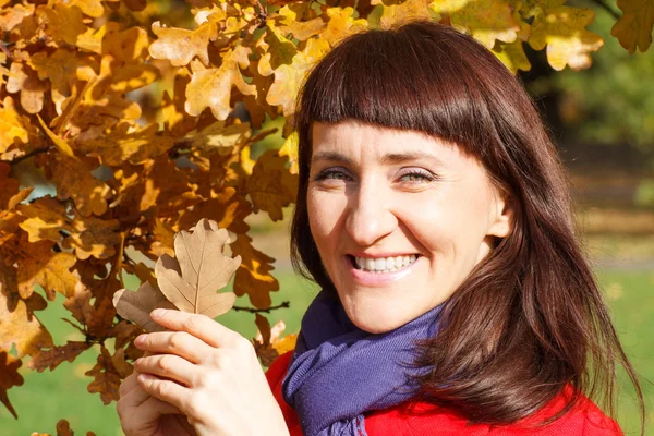 Smiling woman in autumn park with orange leaves in hands — Stock Photo, Image