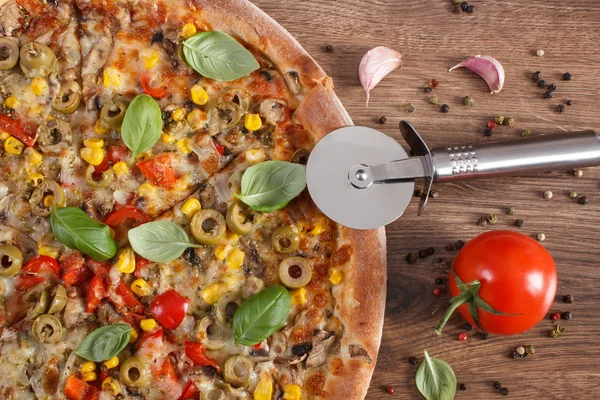 Pizza cutter with vegetarian pizza, ingredients with spices on wooden background, fast food