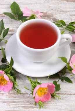 Fincan çay ve eski rustik ahşap arka plan üzerinde yabani gül çiçek