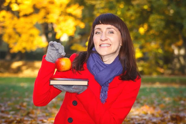 Happy smiling woman holding book and apple in autumn park — Stock Photo, Image