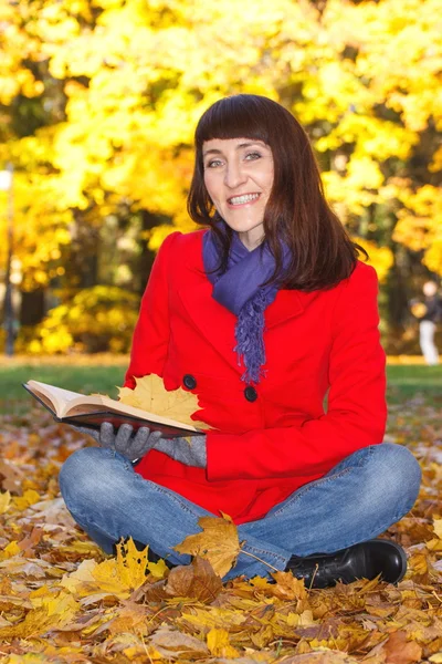 Glücklich lächelnde Frau liest Buch im Herbstpark — Stockfoto