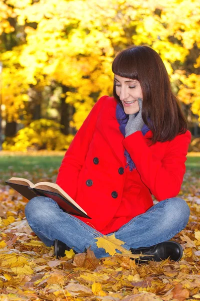 Gelukkig lachende vrouw leesboek in herfst park — Stockfoto