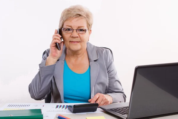 Oudere zakenvrouw praten op mobiele telefoon en werken bij haar Bureau in kantoor, Business concept — Stockfoto