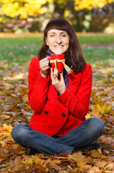 Lachende vrouw in herfst park met warme drank thee of koffie — Stockfoto