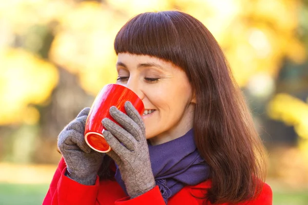 Usmívající se žena v podzimním parku s horkým nápojem čaj nebo kávu — Stock fotografie