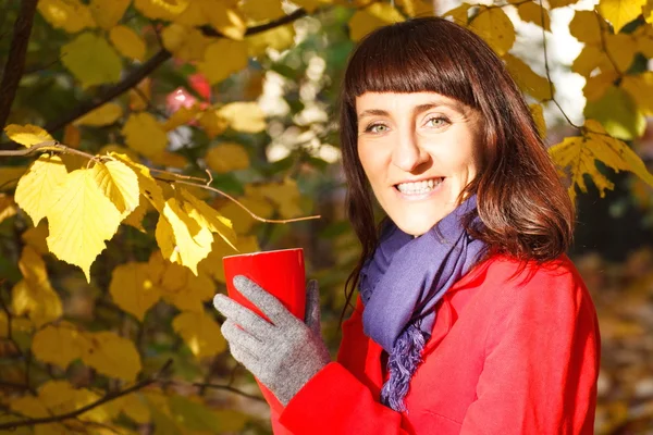 Smiling woman in autumn park with hot drink tea or coffee — Stock Photo, Image